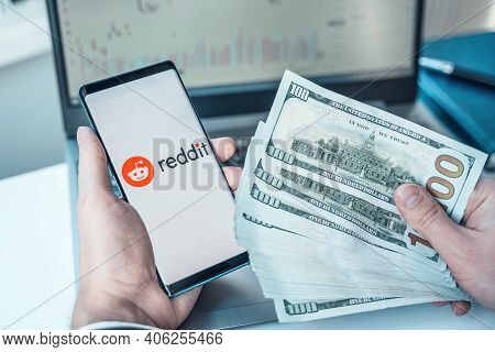 Russia Moscow 02.02.21 Mobile Phone With Logo Of Reddit Traders, Money,dollars In Hands.community Of