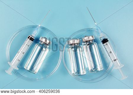 Vials Of Medicine And Syringes In A Petri Dish On A Blue Background. The Covid-19 Coronavirus Vaccin