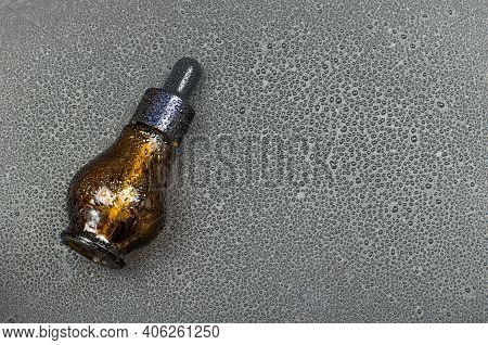 Bottle With Natural Body Oil On A Black Background With Drops Of Foda. Serum In A Glass Bottle. Cosm