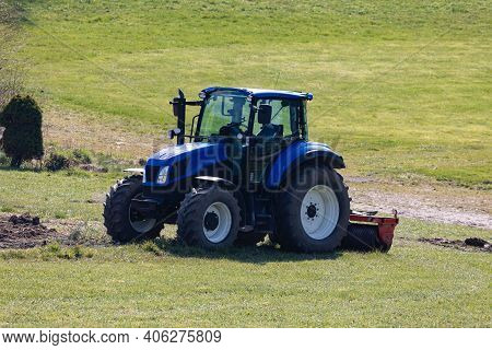 Blue Tractor Ready For Field Work But Without Driver On A Green Meadow, Photographed From Front Side