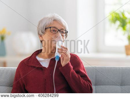 Elderly woman using inhaler for asthma and respiratory diseases at home.