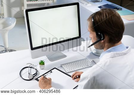 Caucasian male doctor making consultation video call using computer and headset. telemedicine online healthcare during quarantine lockdown.