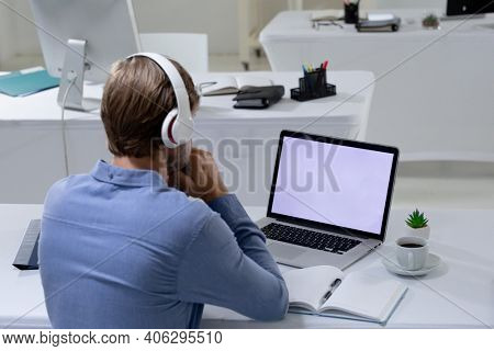 Caucasian businessman having video call meeting using laptop and headphones in empty office. working online, social distancing in the workplace during quarantine lockdown.
