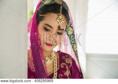 Portrait Asian Woman In A Margenta Indian Tradition Sari, She Is Looking Down At Side A White Wall