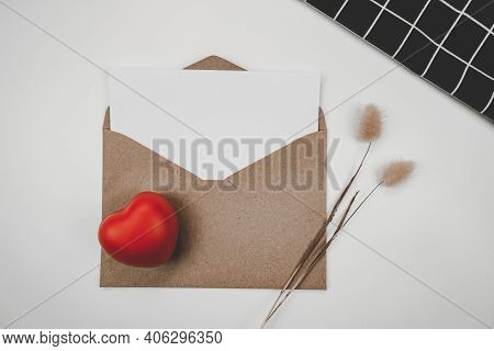 Blank White Paper Is Placed On Open Brown Paper Envelope With Red Heart, Rabbit Tail Dry Flower And