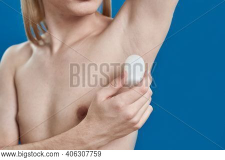 Young Caucasian Man With Long Fair Hair Using Crystalized Deodorant On Armpit While Standing On Blue