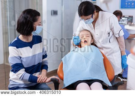 Kid Wearing Dental Bib Sitting On Chair In Dentistiry Office With Mouth Open. Dentistry Specialist D