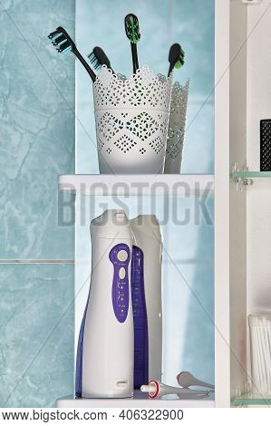 Oral Irrigator Or Water Flosser With Interchangeable Nozzle And Toothbrushes Among Toiletries On Wal