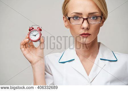 Smiley Nurse Or Doctor Pointing Holding Small Red Alarm Clock Satanding Over Grey Background