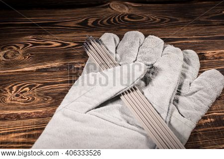 White Leather Welding Glove And Welding Electrodes On A Wooden Background. Studio Photo In Hard Ligh