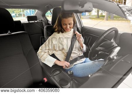 safety, car driving and people concept - happy smiling young woman or female driver fastening seat belt