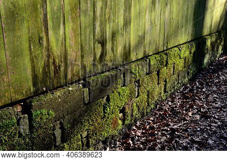 Mossy And Lichen-covered Wall Fences And Wooden Planks. The Blocks Of The Foundation Resemble The Ma