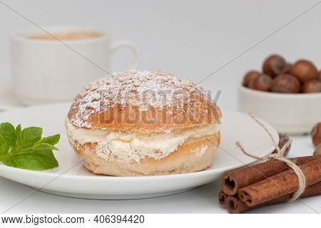 Finnish Shrovetide Bun (laskiaispulla) Close Up On A White Plate With Cinnamon Sticks And Hazelnuts