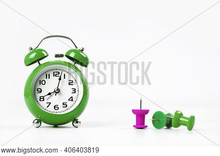 Green Alarm Clock On Grey Office Or Home Desk With Several Drawing Pins With One Of Different Color 
