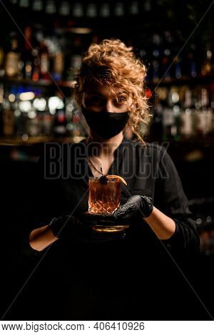 Woman Bartenter In Black Mask And Black Gloves Holding Glass With Cocktail