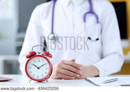 Doctor Therapist Sitting In Office In Front Of Red Alarm Clock Closeup. Doctors Schedule Concept