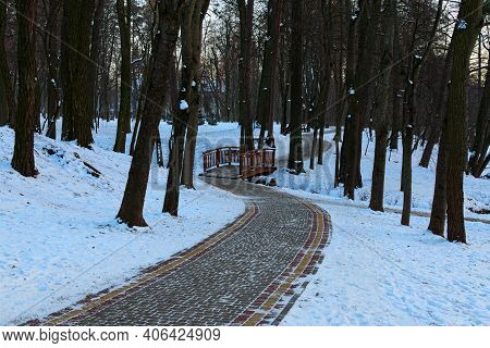 Picturesque Winter Park. Landscape View Of Winding And Narrow Cobbled Pathway With Little Bridge Ove
