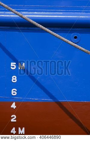 Draft Mark Numbers On Side Of Blue And Red Rust Proof Vessel Hull Behind The Old Giant Fiber Rope In