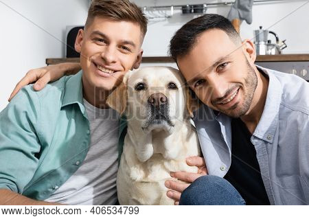 Happy Same Sex Family Smiling Near Labrador At Home.