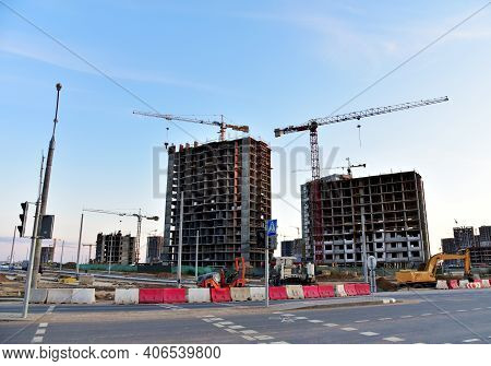 View On The Large Construction Site With Tower Cranes And Buildings On Sunset Background. Road Work 