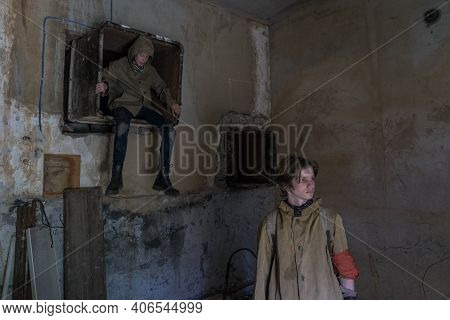 Boys Standing In An Abandoned Building. Wandering Boy. Man In A Protective Cloak With A Hood. Post A
