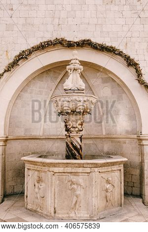 A Bowl With A Fountain In Patterns Of Stone Near The Stone Wall Under The Arch. Street Fountain In T