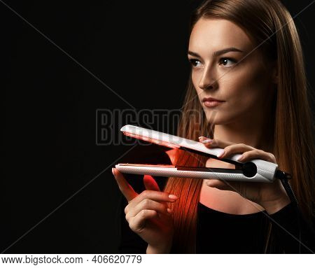 Portrait Of Young Refined Woman Holding Modern Hair Straightener In Hands And Looking Aside At Copy 