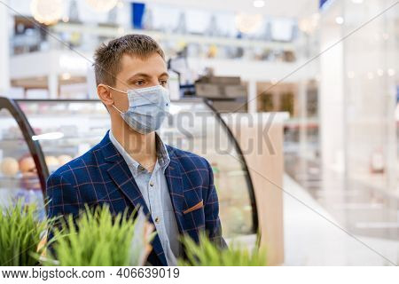 A Young Man In A Jacket Sits In A Cafe In A Medical Mask With A Phone In His Hand