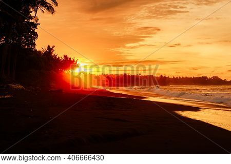 Warm Sunset Or Sunrise With Ocean Waves And Palms At Black Sand Beach In Bali