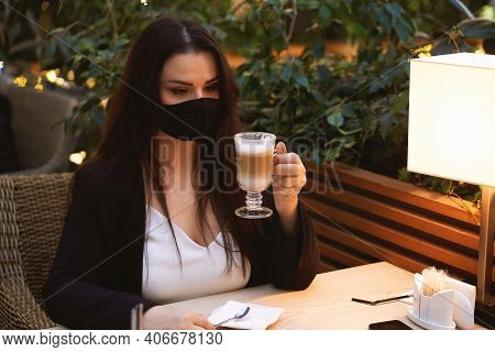 Young Brunette Woman In Medical Mask Drinkingcoffee Latte In Cafe