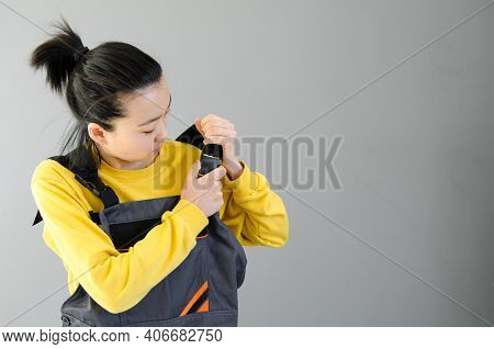 Female Construction Worker Dressed In Special Clothes With A Cordless Screwgun, A Construction Tool 