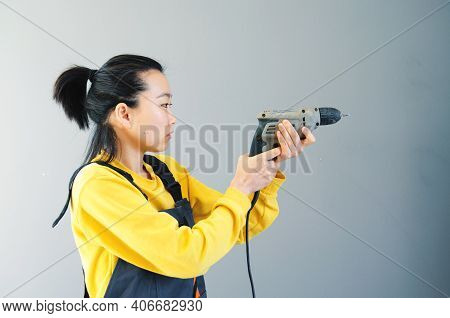 Female Construction Worker Dressed In Special Clothes With A Cordless Screwgun, A Construction Tool 