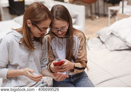 Teenage Giel Showing Something On Her Smart Phone To Her Mom