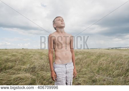 Boy In Shorts Stands In The Field. Boy Looks To The Sky. Dreamer Guy