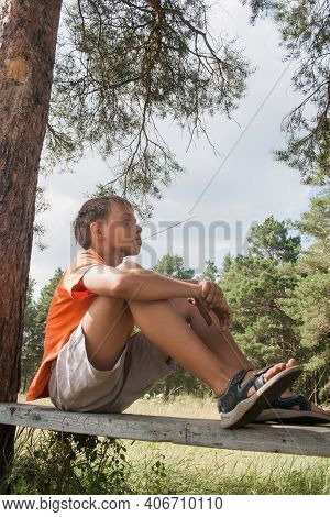 Two Boys In Shorts Sit On A Bench Under A Tree. Boy Looks To The Sky. Dreamer Guy