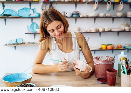 Mid-shot Of Potter Decorating Clay Mug After Firing In Oven. Woman In White Tanktop Enopying Creativ