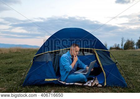 Man Working On Laptop In Tent In Nature. Young Freelancer Sitting In Camp. Relaxing In Mountains. Re