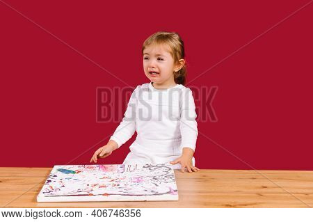 Little Girl Crying Sitting At The Wooden Table With Canvas Picture Set. Unpatient Toddler Girl Waiti