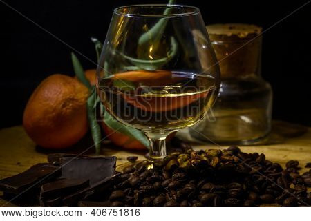 Glass Of Brandy On Wooden Table With Close Chocolate, Coffee And Mandarins.