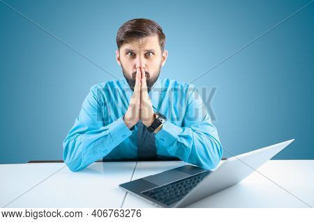 A Bearded Businessman At A Computer Prayerfully Folded His Hands In Front Of Him, A Man In A Shirt A