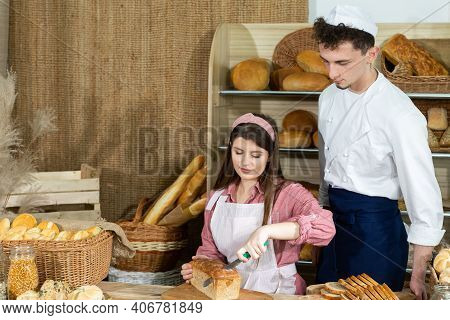 A New Clerk Learns To Cut The Bread Properly Under The Bakers Supervision. An Attractive Saleswoman 