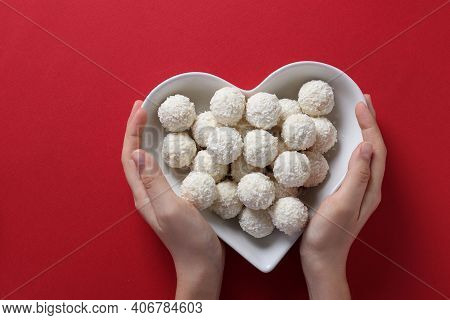 Sweet Coconut Rafaello Candies In A Heart-shaped Plate In Female Hands On A Red Background. View Fro