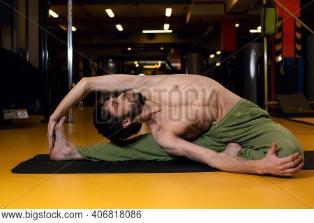 A Young Man Performs A Complex Position Parivritta Janu Shirshasan. Professional Yoga. An Inverted T