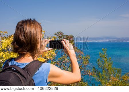 A Woman Hiker With A Backpacker Taking A Photo Of The Sea With Her Smartphone. Strunjan, Slovenia