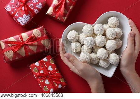 Sweet Coconut Rafaello Candies In A Heart-shaped Plate In Female Hands, And Gift Boxs On A Red Backg