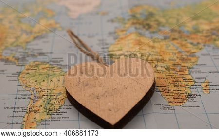 A Wooden Heart Over A Global Map With Copy Space. Top View. Flat Lay. Selective Focus.