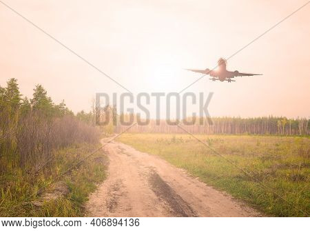 Plane Over A Sand Road In A Green Field Near The Forest. The Sun Is Shining