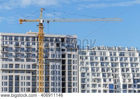 Tower Crane Construction On The Background Of A Completed Apartment Building And Blue Sky.  A Glut O