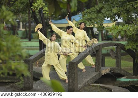 Group Of Beautiful Young Asian Women Practicing Tai Chi With Fans On The Bridge In The Park Wearing 