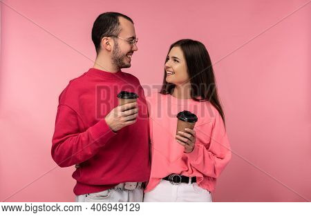 Photo Of Attractive Man Wih Beard In Red Clothing And Woman In Pink Holds Coffee And Gawp On Each Ot